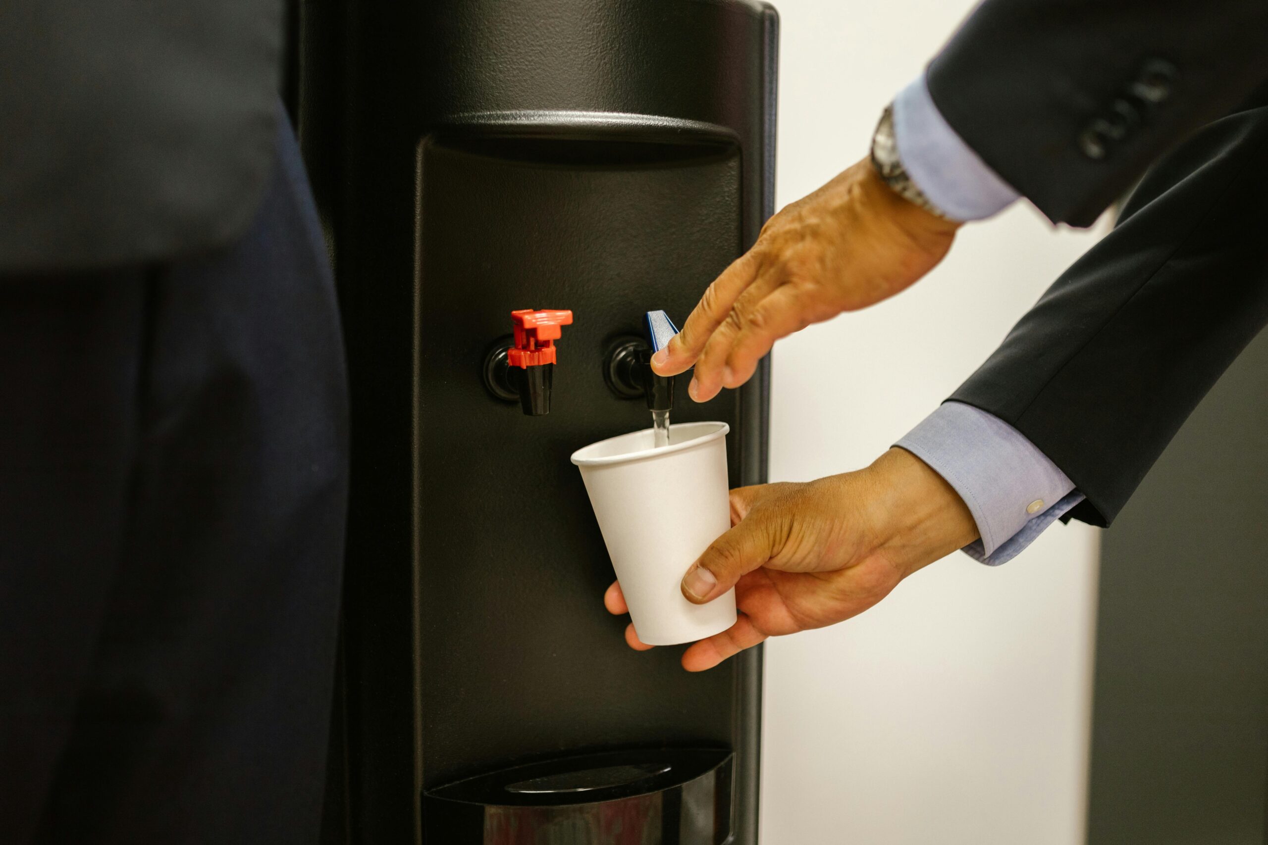 man using water dispenser in office sc - pexels